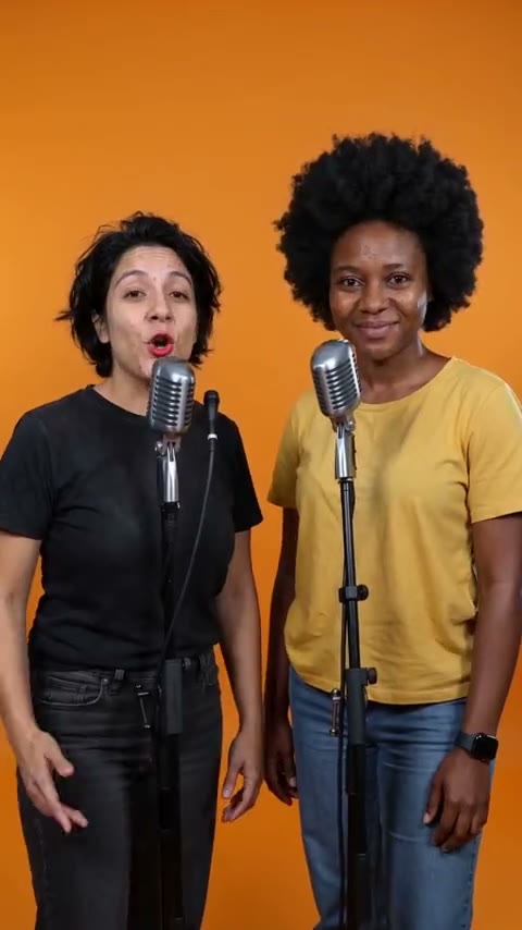 Two performers at microphones against an orange backdrop
